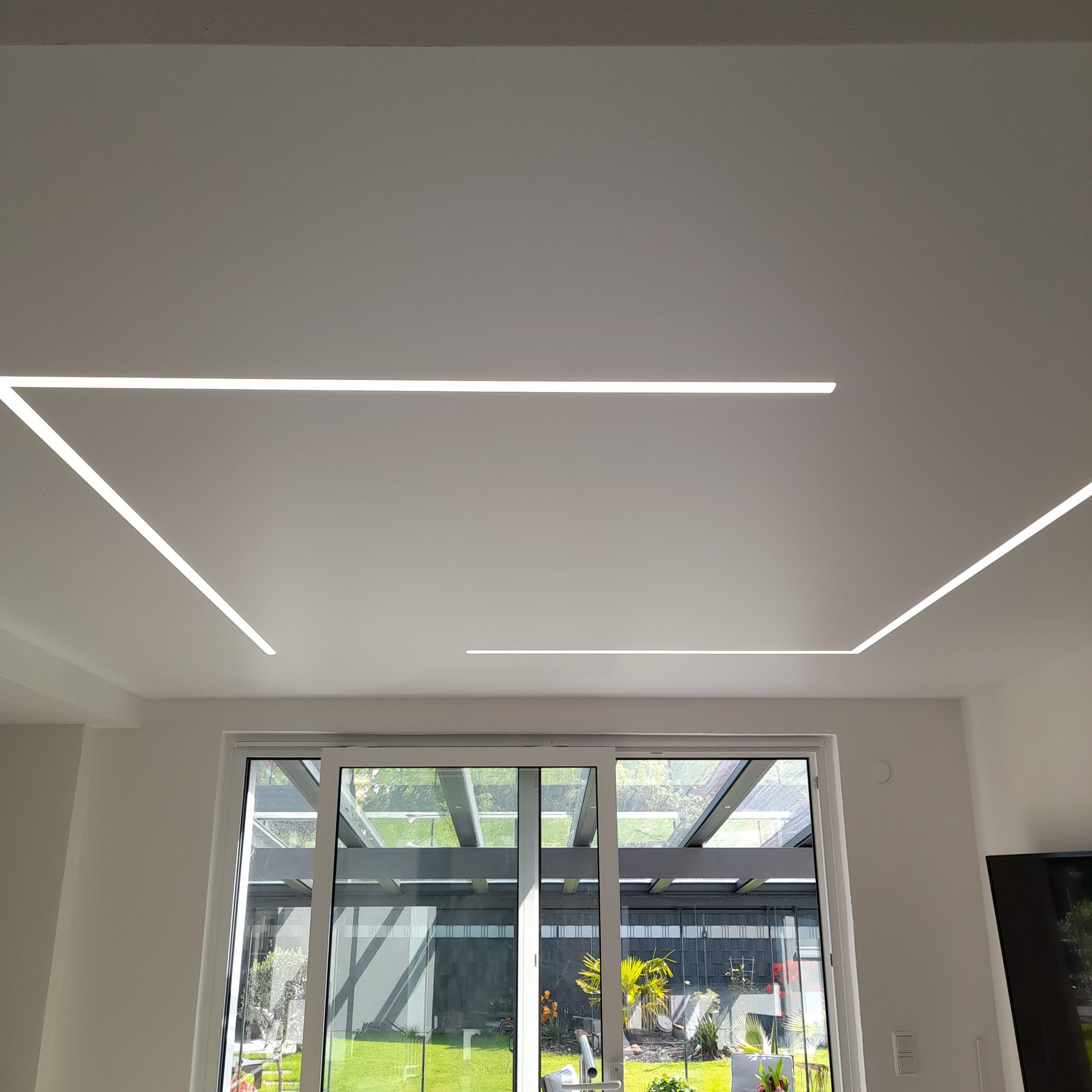Heller Wohnraum mit geometrischen Lichtlinien in der Spanndecke und Zugang zum Garten