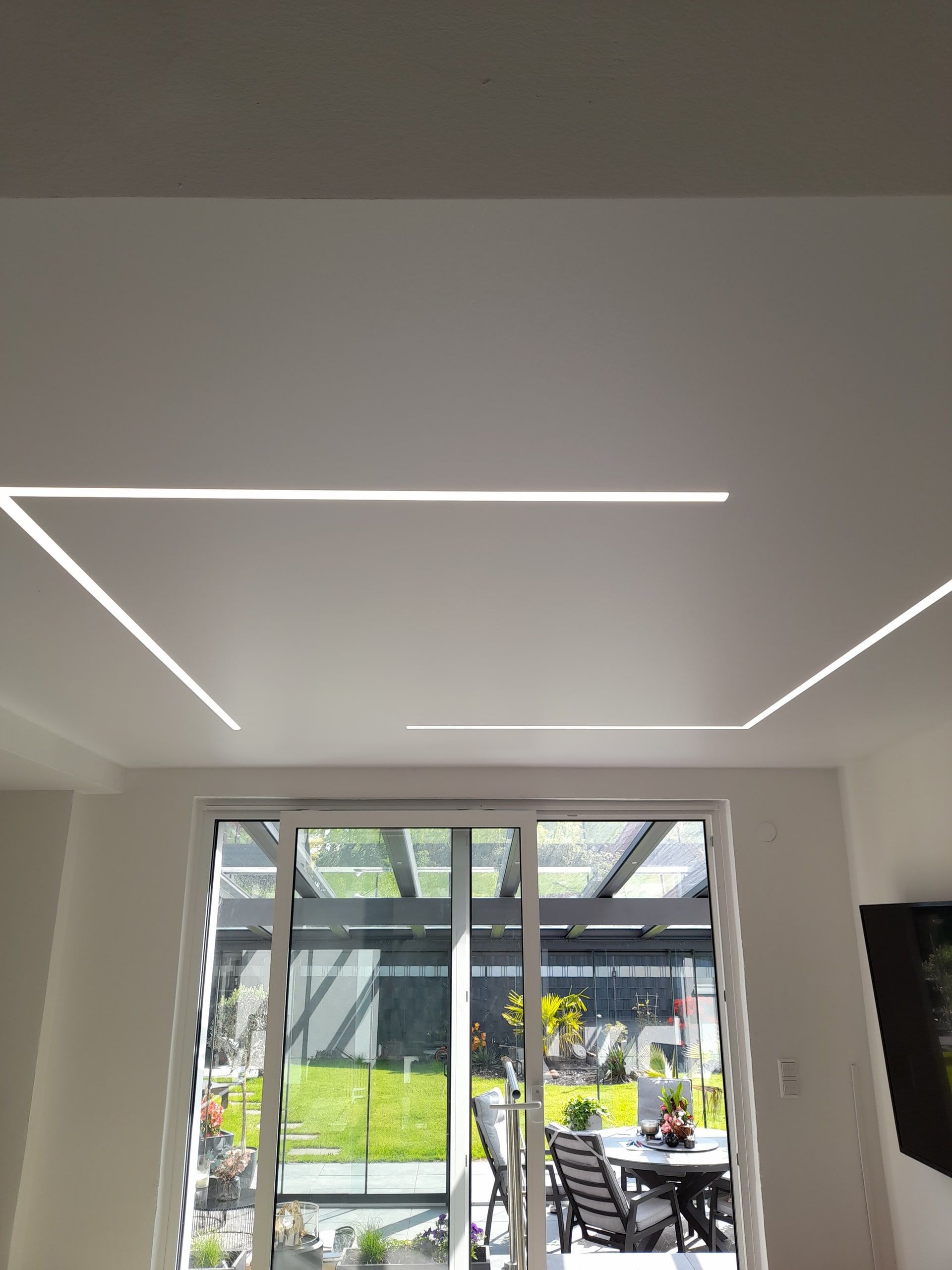 Heller Wohnraum mit geometrischen Lichtlinien in der Spanndecke und Zugang zum Garten